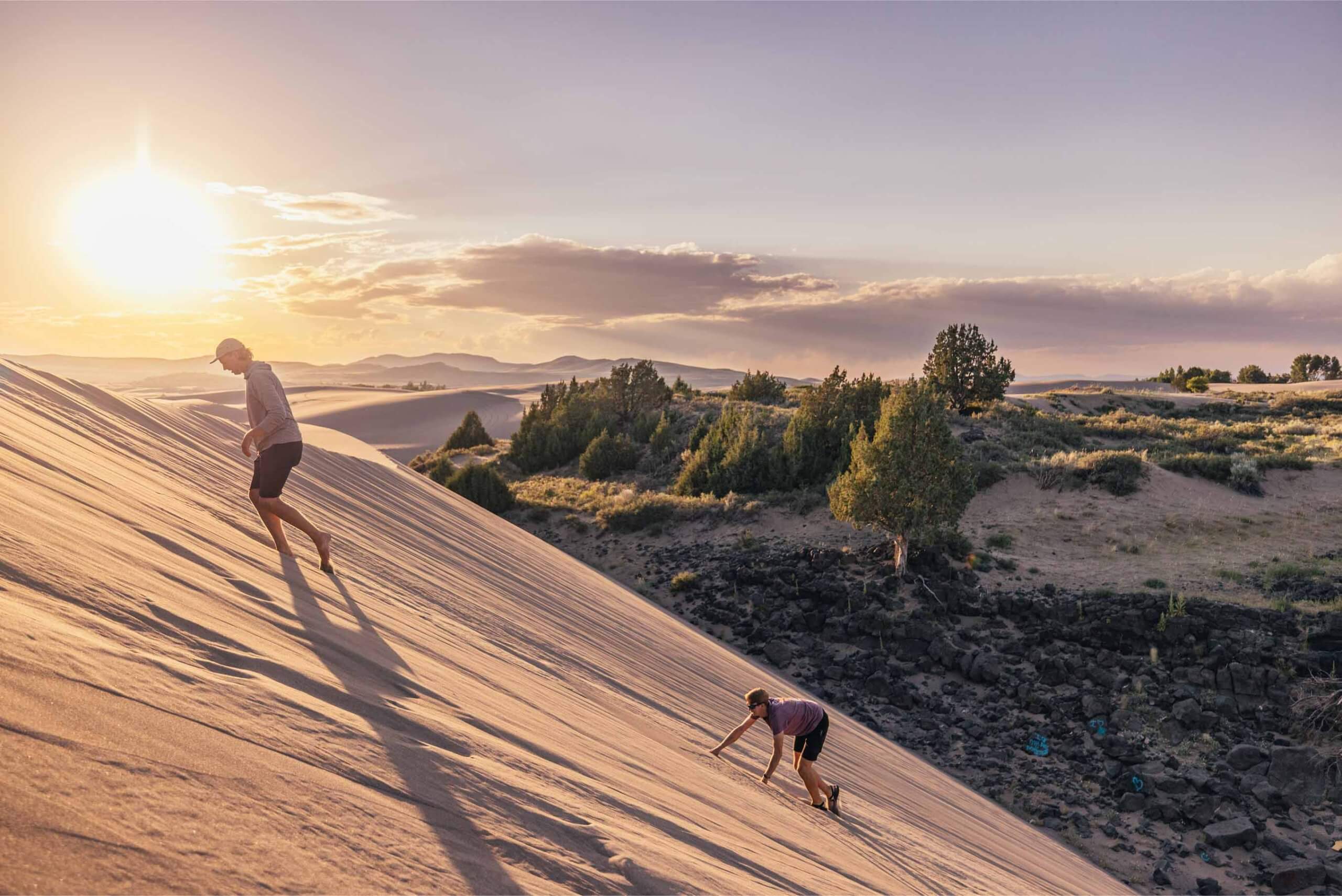 Two travelers walk up the St. Anthony Sand Dunes at sunset.