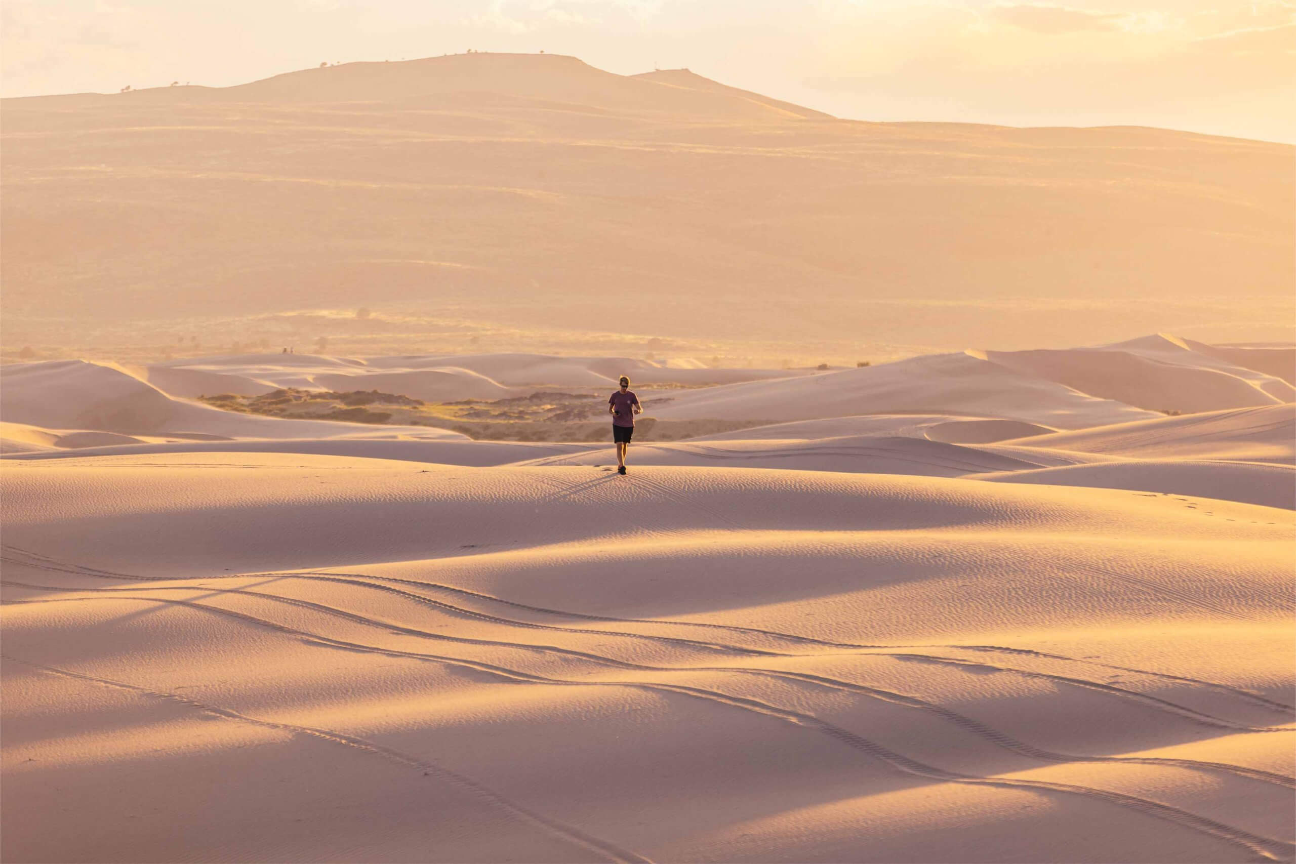 A glimpse from a distance of a traveler walking, exploring the St. Anthony Sand Dunes at sunset.