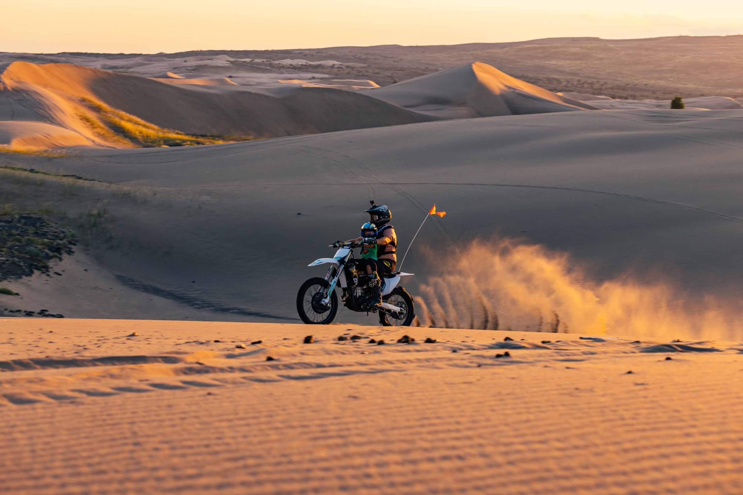 A traveler rides a fat tired bike, revving up dust at the St. Anthony Sand Dunes at sunset.