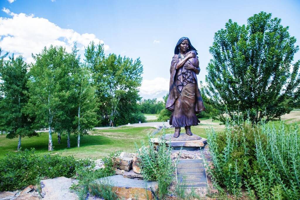 A bronze statue of Sacajawea stands outside the Sacajawea Interpretive Center surrounded by trees.