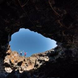 Two people raise their arms at the edge of a lava tube.