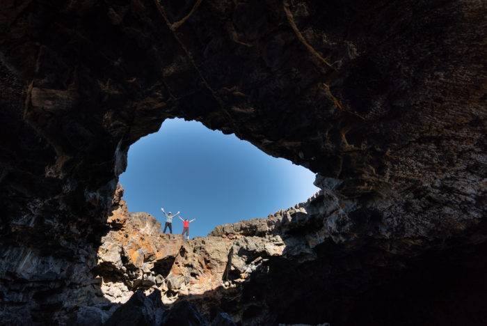 A family standing at the edge of a hole in a cave at Craters of the Moon National Monument & Preserve.