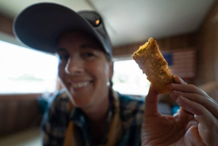 A woman wearing a baseball cap holding a fried pickle inside the Pickle's Place restaurant.