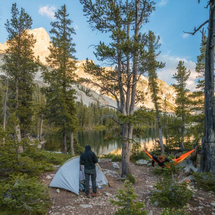 man standing next to a tent in the mountains