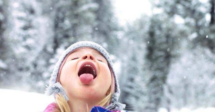 A little girl catching a snowflake on her tongue.