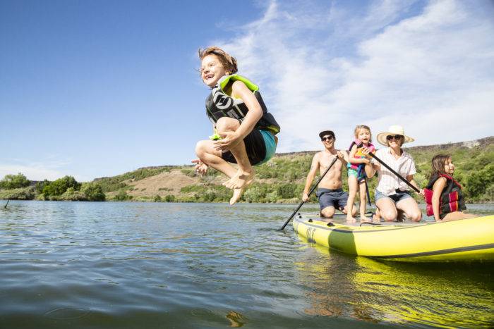 A child jumping off the paddle board into the Snake River to swim.