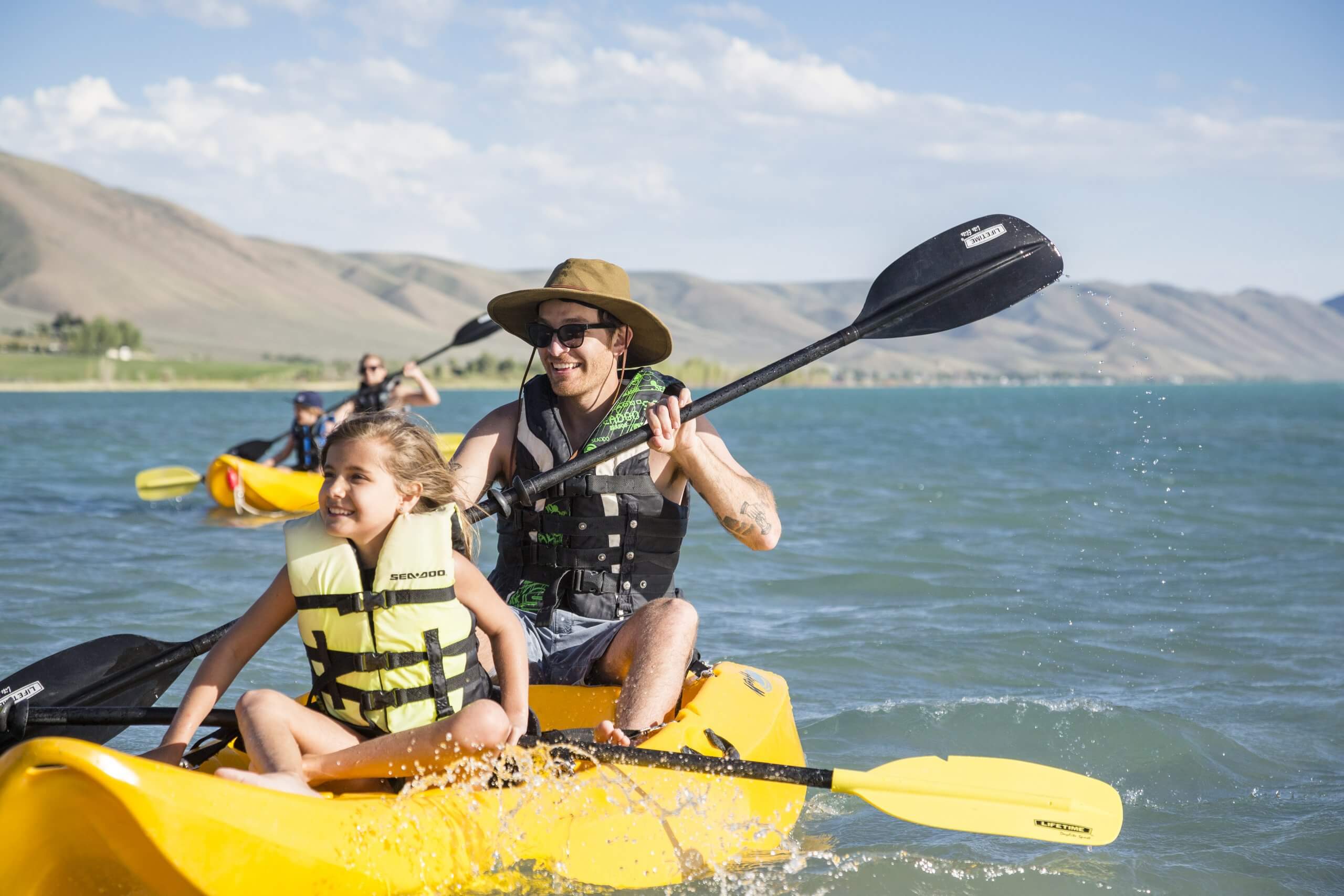 A father and daughter kayaking on Bear Lake, with mountains in the distance.