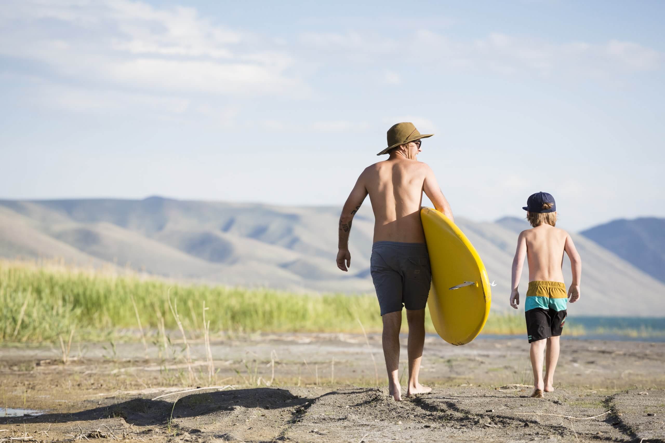 A father and son walking to the lake with their paddle board.