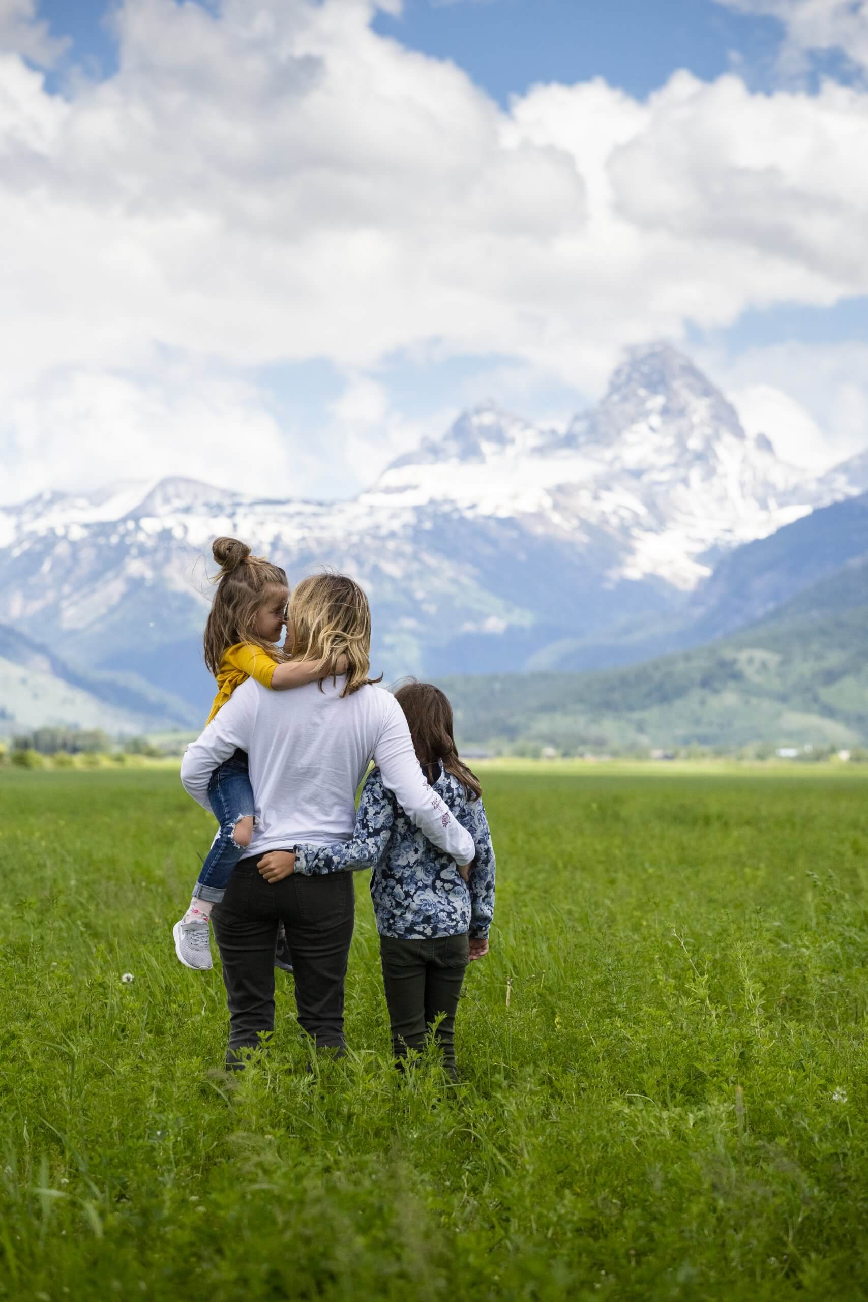 A mother and her children standing in a field admiring the Teton Mountains.