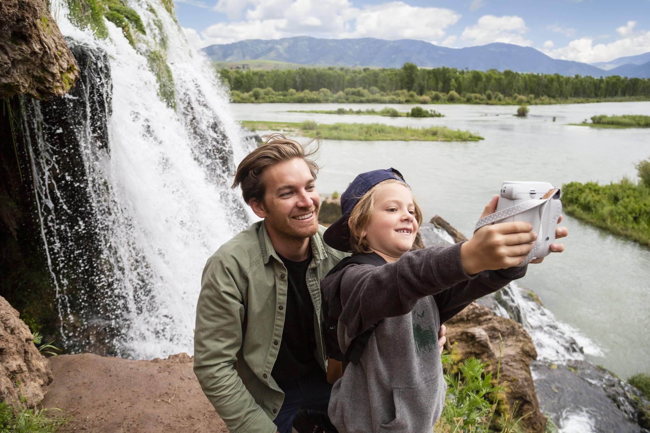 A father and son taking a picture near a waterfall.