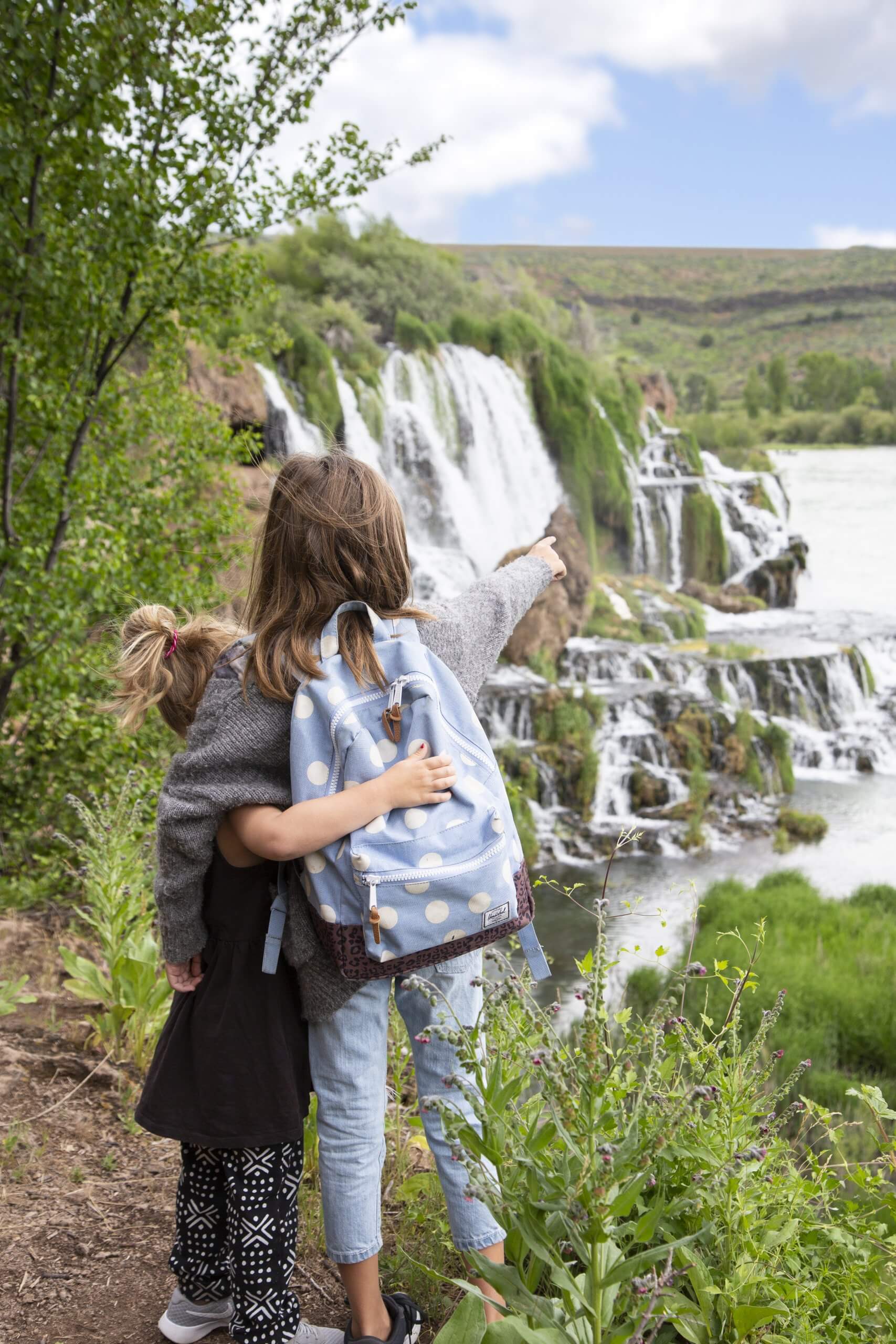 Two girls standing near a waterfall.