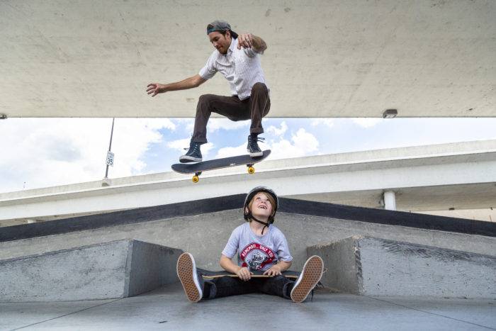 A father jumping over his son at a skate park.