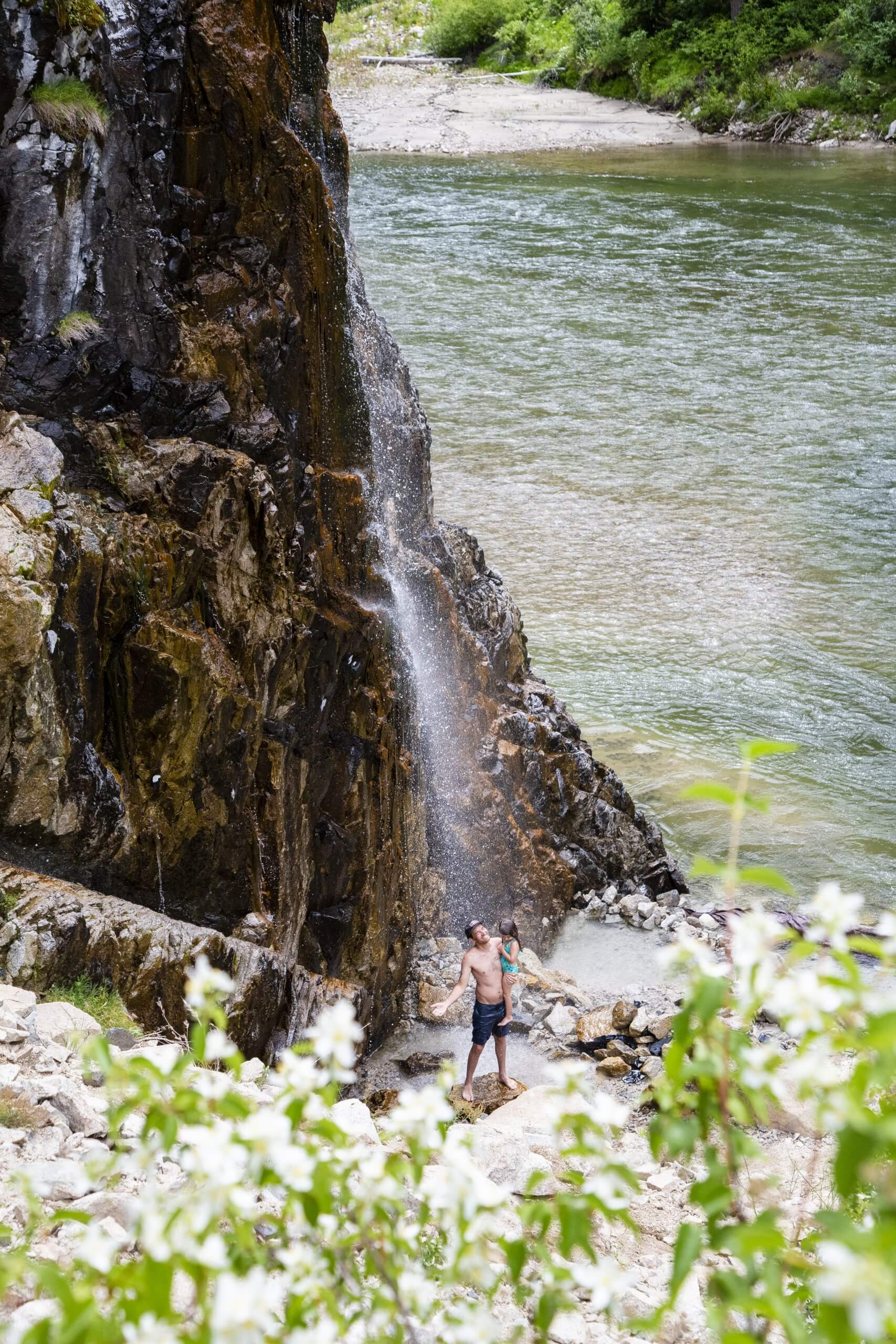 A father and daughter standing in a hot springs near a river.