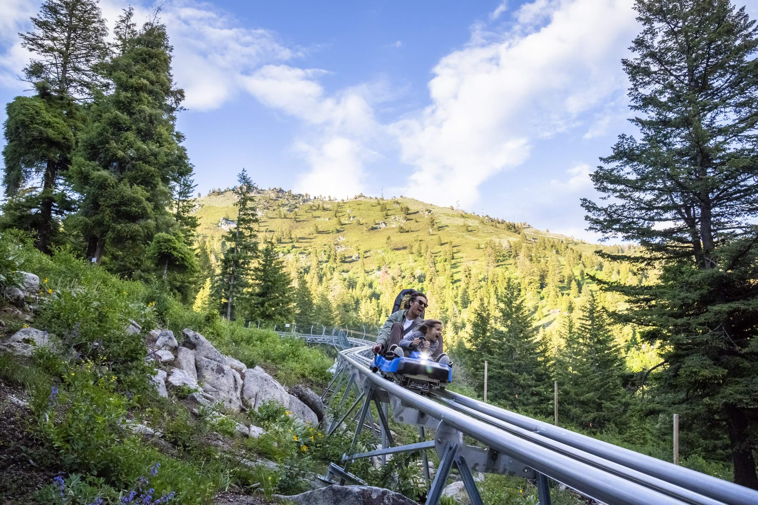 a father and son ride smile as they ride down a mountain coaster