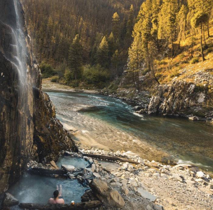 A person sitting in a hot springs near a river.