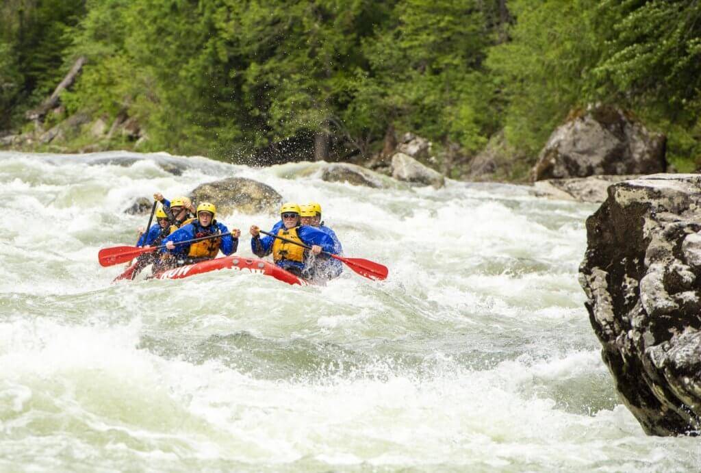 Six people raft down a rapid on a river in a red raft.