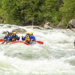 Six people raft down a rapid on a river in a red raft.