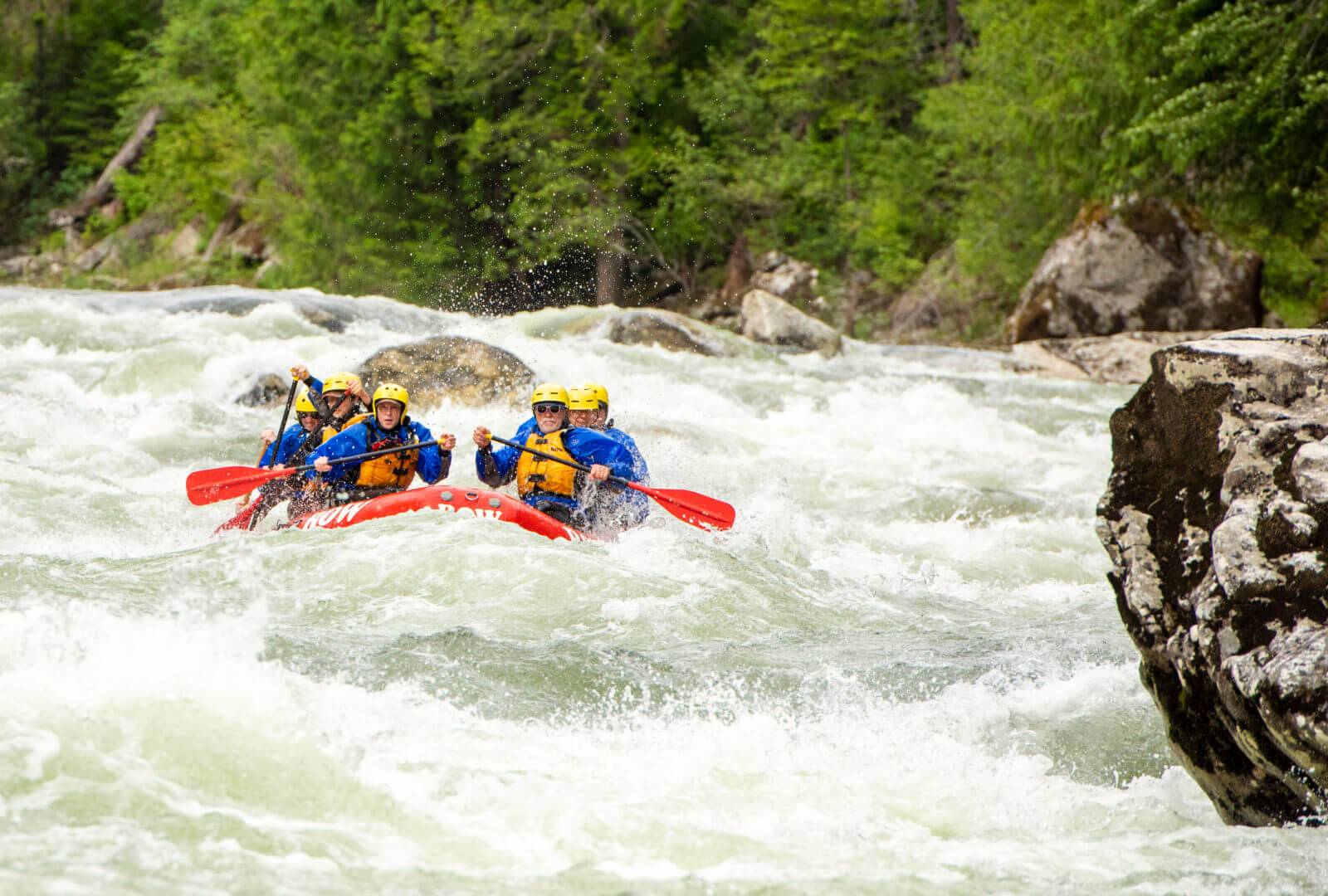 Six people raft down a rapid on a river in a red raft.