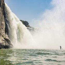 man paddleboarding by a waterfall