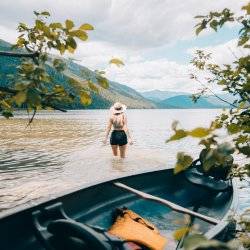 Woman standing in lake water in front of a canoe facing view of mountains.