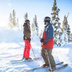 A couple facing each other on the powder in front of trees at Pomerelle Mountain Resort.