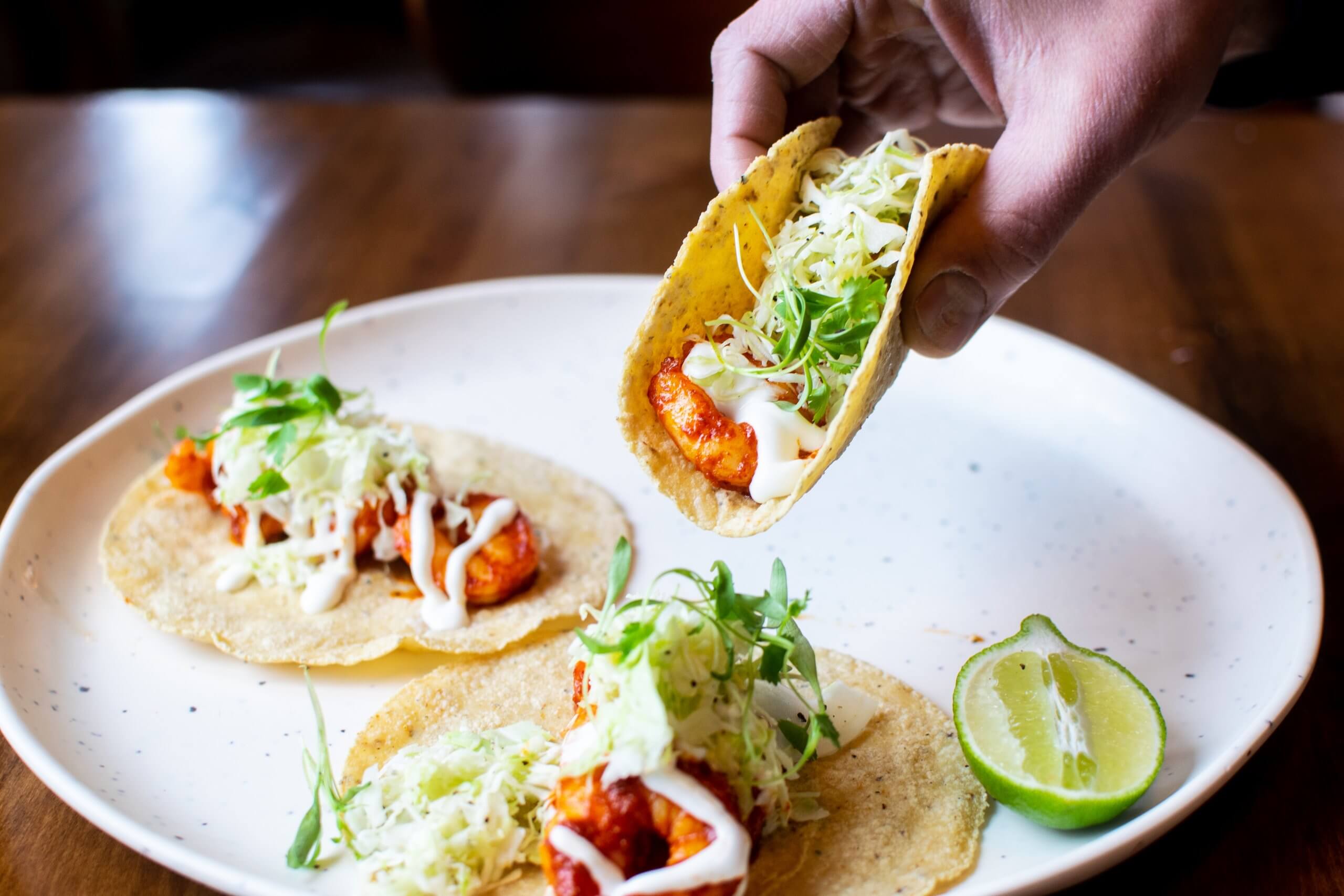 A person holds a taco over a plate of tacos.