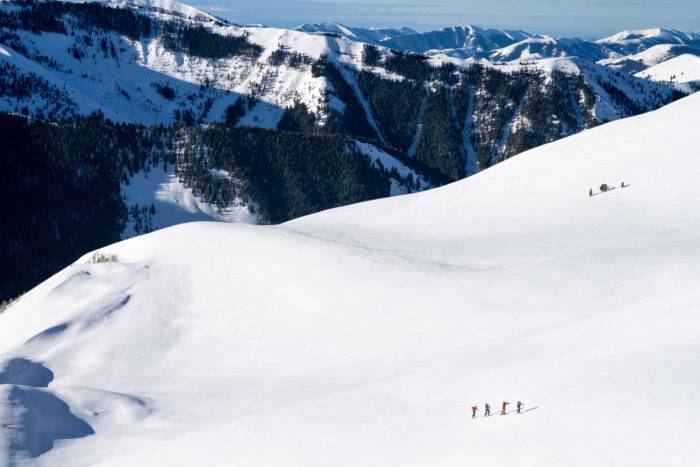 An aerial view of a group of skiers on a snowy slope in front of mountains. 