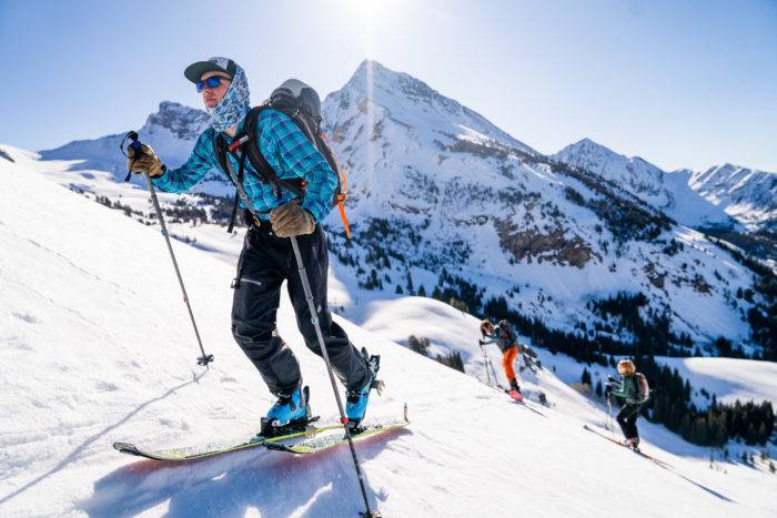 Three people backcountry skiing across a slope uphill. 