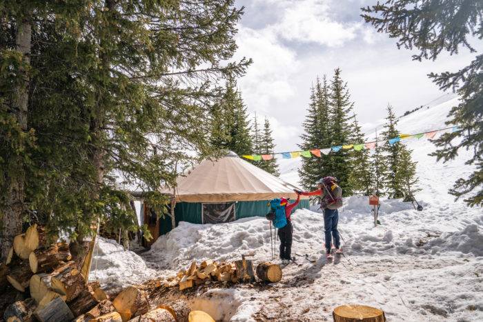 Two skiers standing by yurt outside. 