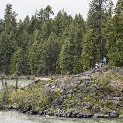 People standing on rocks overlooking Priest Lake with trees in the background.