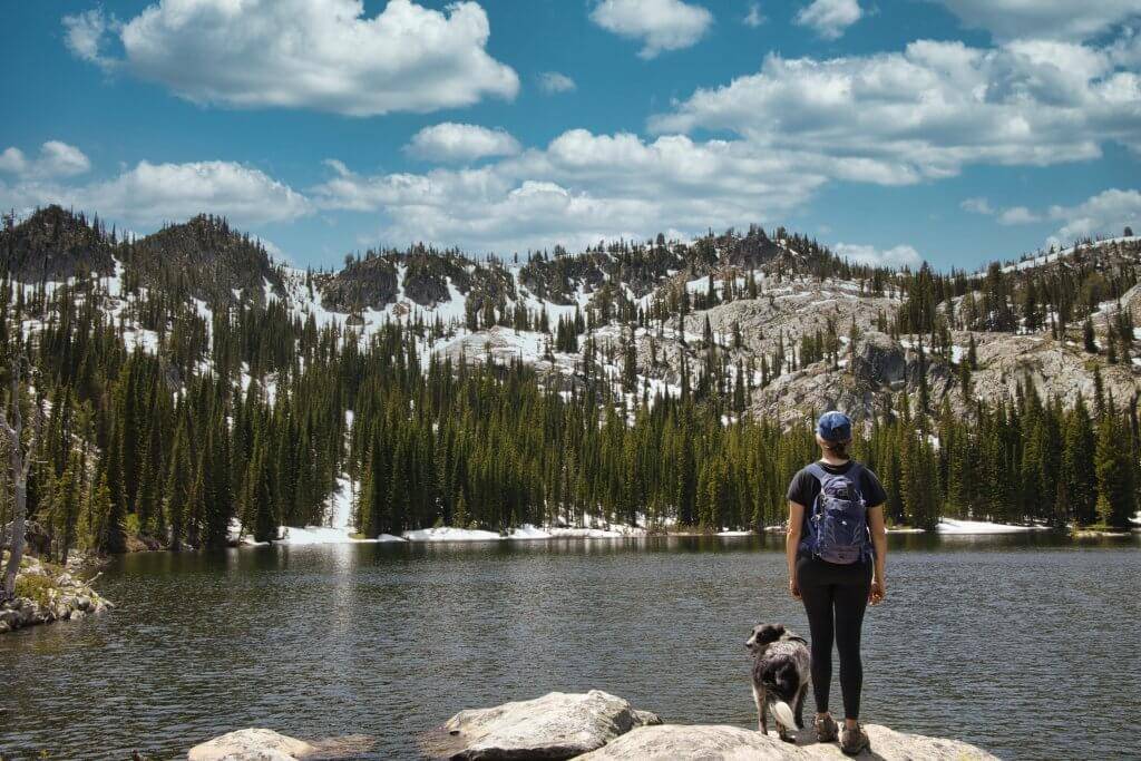 A backpacker and their dog stand before Blue Lake in Cascade, rugged landscape in the distance.