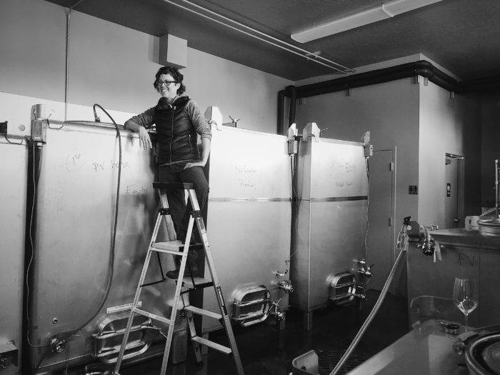 woman on ladder next to wine fermentation tanks