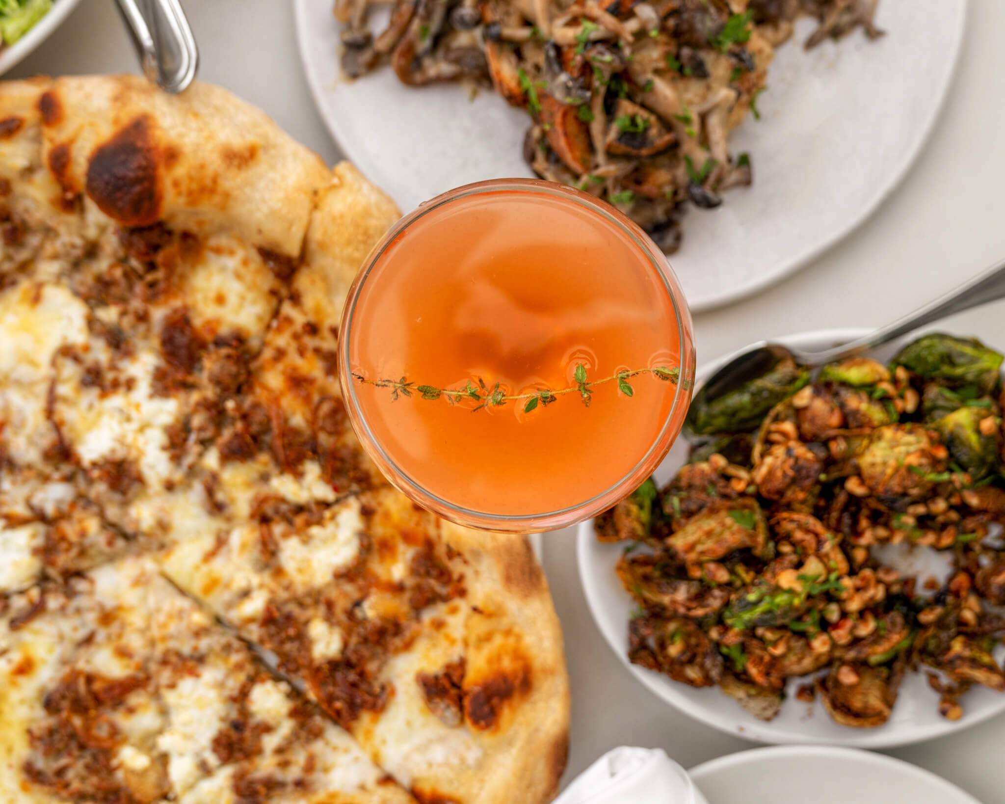 pizza, cocktail, and brussel sprouts on a table