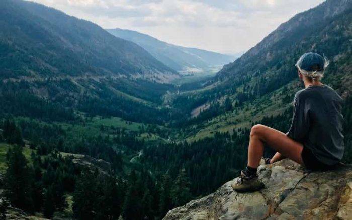 woman sitting on a rock looking at a tree-covered valley