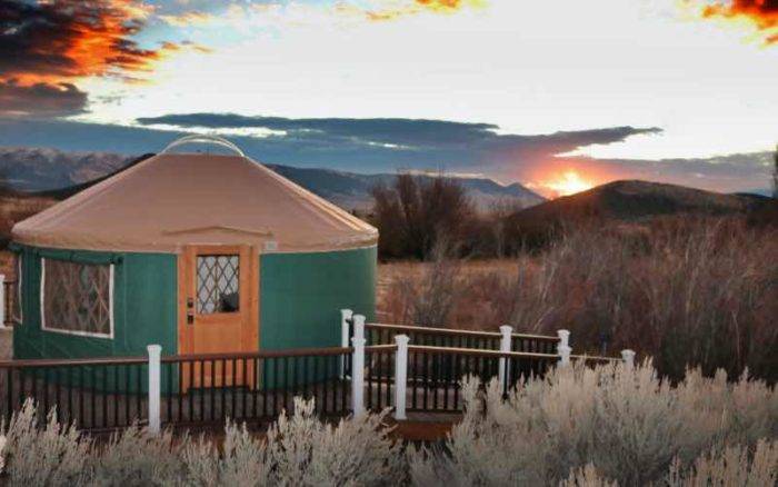 glamping yurt surrounded by trees and the sun setting over mountains in the distance