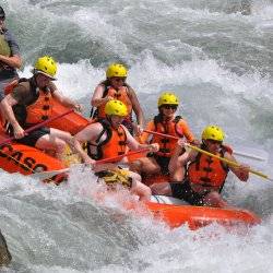 Six people on orange water raft hold up their oars as large whitewater waves rise around them on the Payette River.