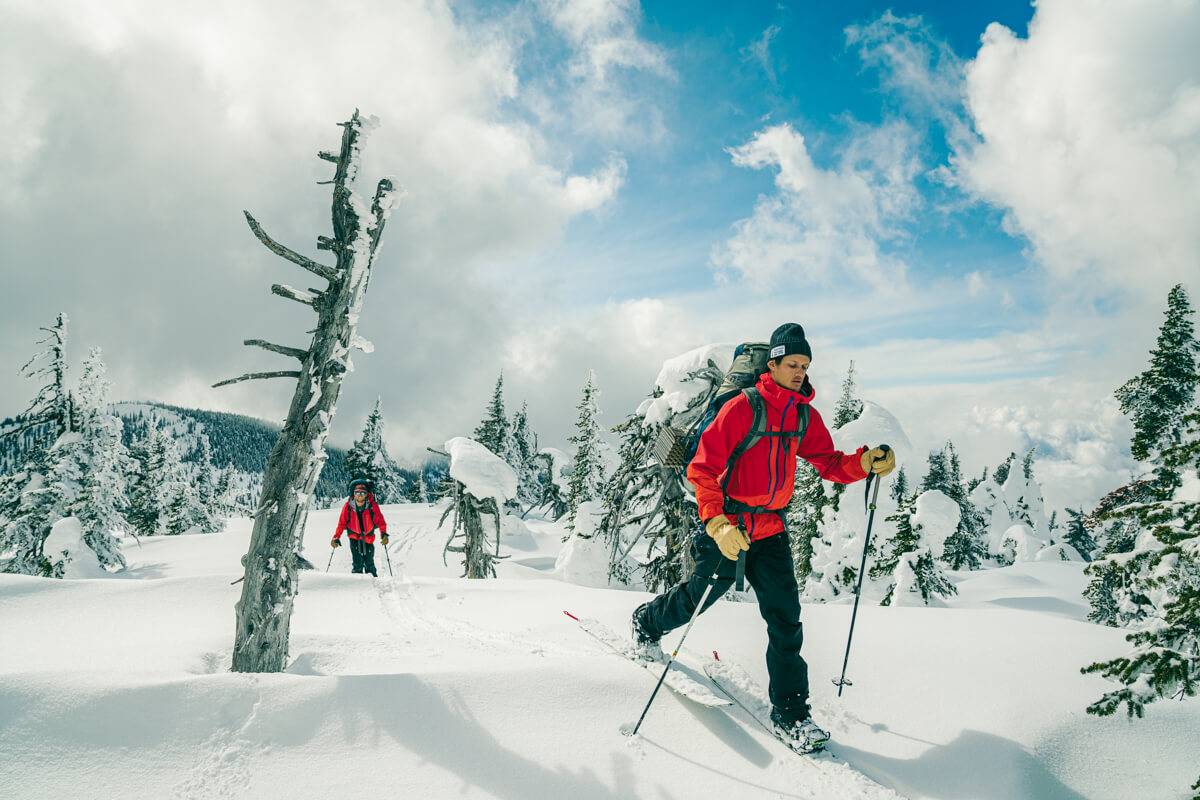 Two people in red jackets on skis traversing across snow.