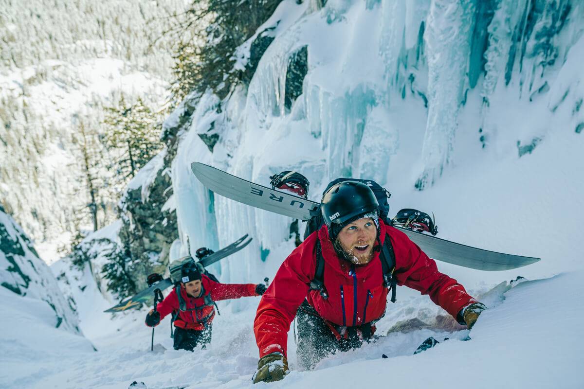 Two people in red jackets scaling a snow covered mountainside.