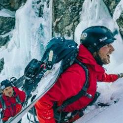 2 people in red jackets scaling a snow covered mountainside