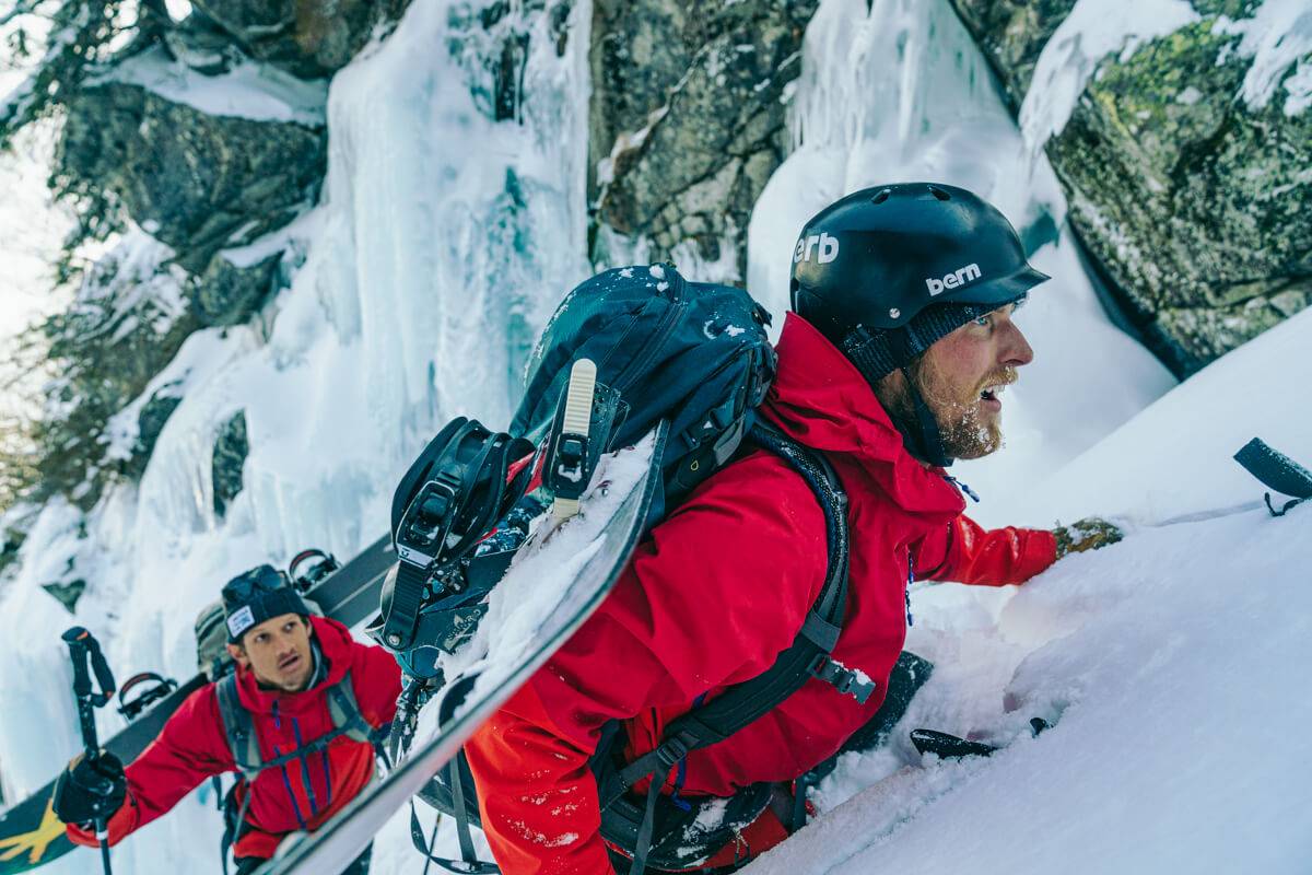 2 people in red jackets scaling a snow covered mountainside