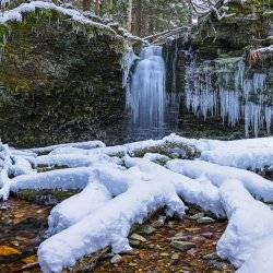 A view of the frozen waters of Shadow Falls with snow covered rocks and icicles in the foreground.