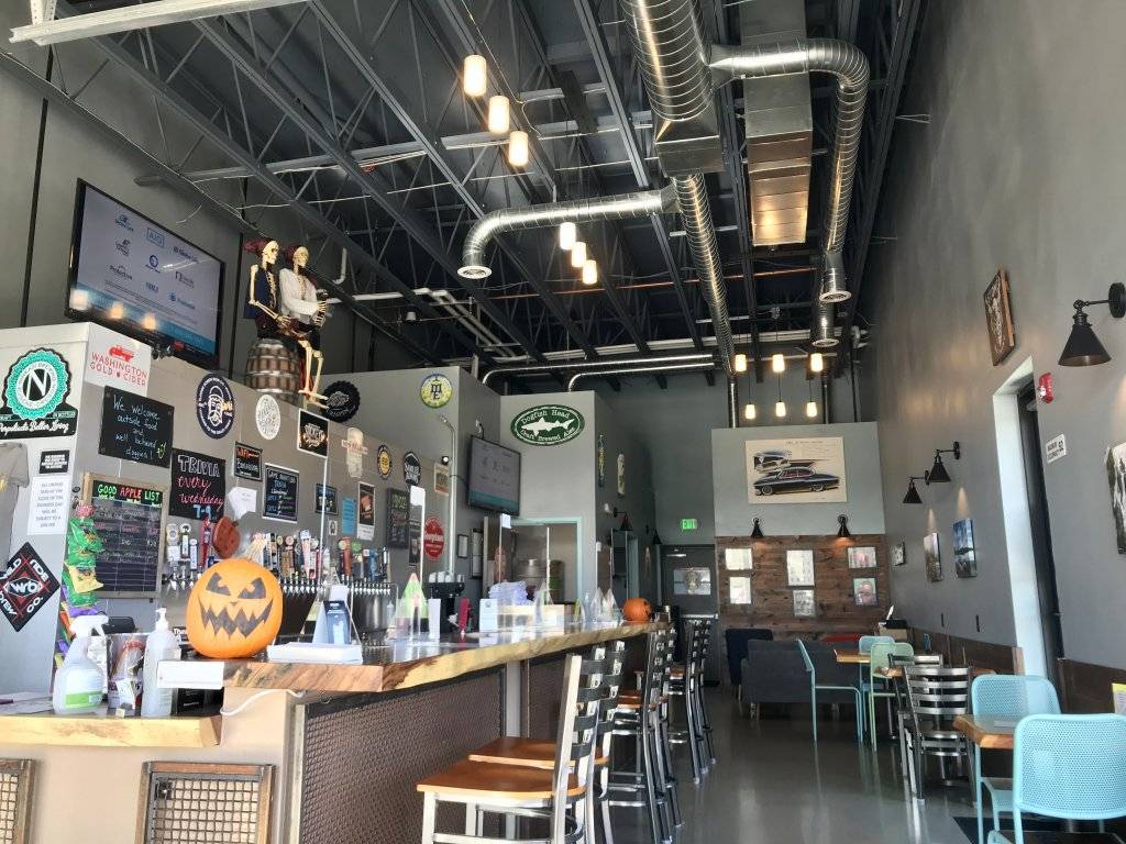 interior view of Good Apple Taphouse, with a bar and bar stools on the left and table and chairs along the right wall
