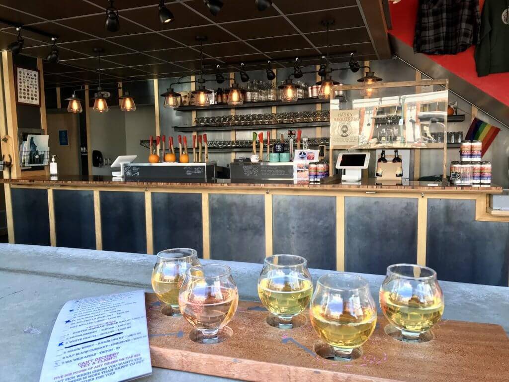 a menu and a flight of five ciders on a table with a bar in the background