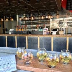 A menu and a flight of five ciders on a table with a bar in the background.