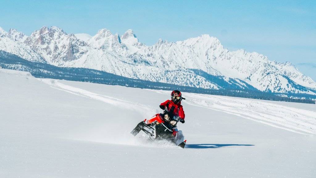 man on snowmobile with sawtooth mountains in background