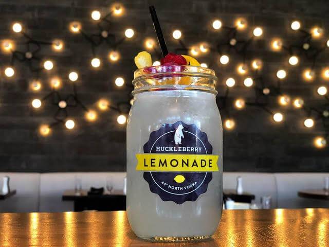 a lemonade cocktail in a jar topped with fruit on a table with booths in the background