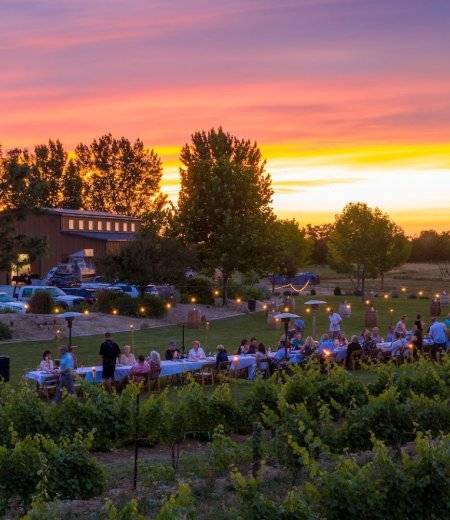 A vibrant sunset of purple, pink and orange sets behind a barn at Huston Vineyards