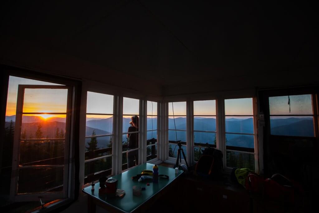 woman standing outside a fire lookout looking at sunset