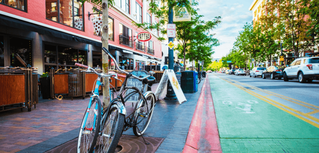 two bikes leaning against a tree on the sidewalk outside of a restaurant alongside a busy street