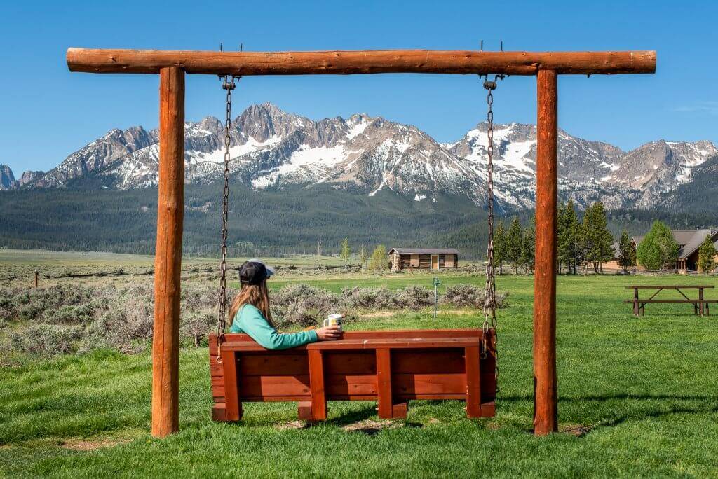 woman sitting on wooden swinging bench looking at Sawtooth Mountains